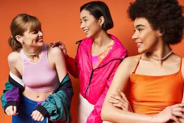 Un groupe diversifié de femmes d'origines ethniques différentes debout ensemble, respirant la force et l'unité sur un fond de studio orange. — Photo de stock