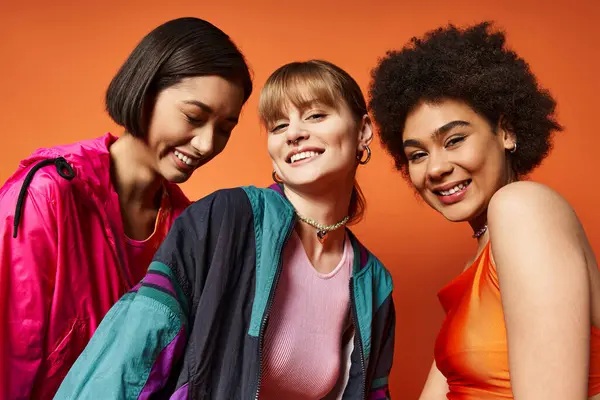 Drei schöne Frauen verschiedener Ethnien stehen zusammen vor orangefarbener Kulisse. — Stockfoto