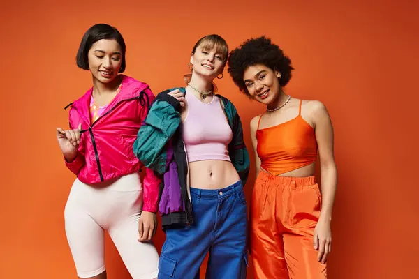 Three beautiful, multicultural women of Caucasian, Asian, and African American descent stand together on an orange background. — Stock Photo