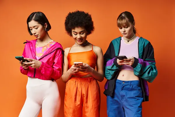 Un grupo diverso de tres mujeres, incluyendo caucásicas, asiáticas y afroamericanas, de pie juntas, absortas en sus teléfonos celulares. - foto de stock