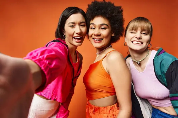 Разнообразная группа женщин, в том числе кавказская, азиатская и афроамериканская, стоят вместе на ярком оранжевом фоне студии. — стоковое фото