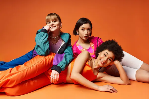 A diverse group of women, including Caucasian, Asian, and African American, laying on top of each other in a studio on an orange background. — Stock Photo