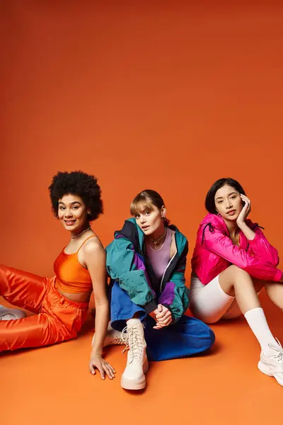 Un gruppo eterogeneo di giovani donne siedono insieme, mettendo in mostra la bellezza multiculturale su uno sfondo arancione. — Foto stock