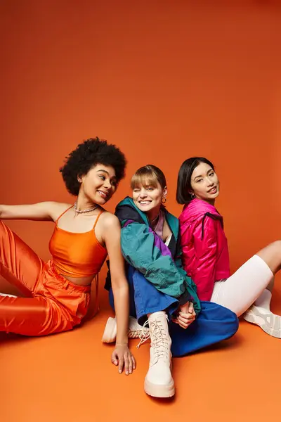 A group of beautiful young women of different ethnicities sitting closely together in a studio against an orange background. — Stock Photo