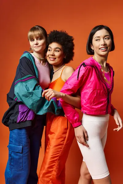 Un groupe de belles femmes multiculturelles se tiennent ensemble sur un fond de studio orange, exprimant confiance et solidarité. — Photo de stock