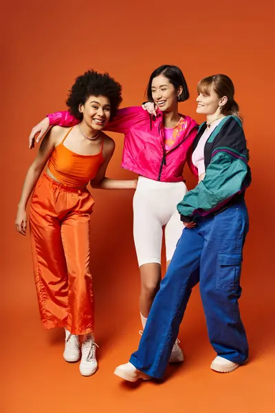 Tres mujeres de diferentes orígenes étnicos se unen en un estudio sobre un fondo naranja, mostrando belleza en la diversidad. - foto de stock