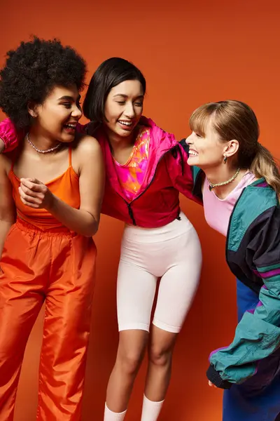 Eine Gruppe junger Frauen verschiedener Ethnien und Herkunft, die solidarisch in einem Studio mit orangefarbenem Hintergrund zusammenstehen. — Stockfoto