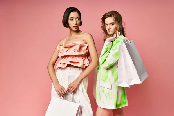 Duas mulheres, representando a diversidade, ficar segurando sacos de compras contra um fundo de estúdio rosa. — Stock Photo