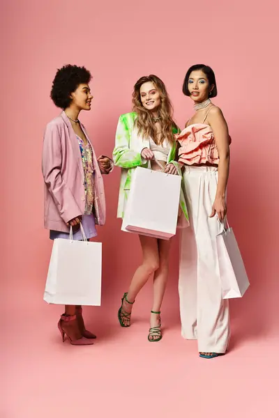Three diverse women holding shopping bags in a studio against a pink background, symbolizing fun and fashion. — Stock Photo