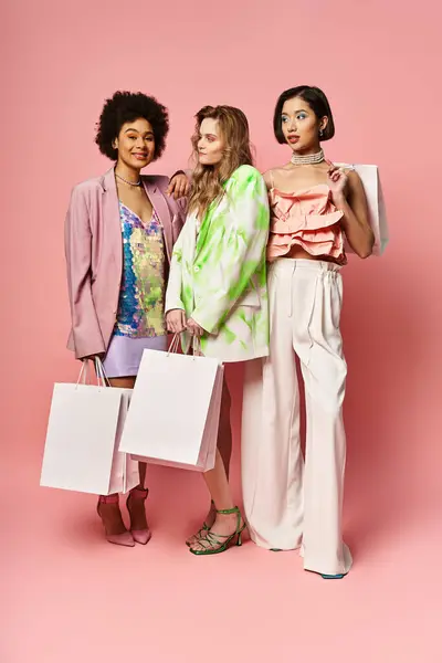Trois femmes diverses, caucasiennes, asiatiques et afro-américaines, debout ensemble, tenant des sacs à provisions sur un fond de studio rose. — Photo de stock