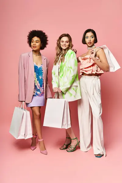 Drei unterschiedliche Frauen stehen zusammen und halten Einkaufstüten vor rosa Hintergrund und strahlen Freude und Zufriedenheit aus.. — Stockfoto