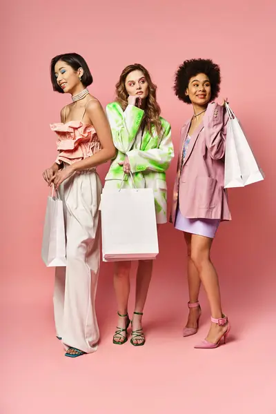 Three diverse women holding shopping bags against a pink studio background. — Stock Photo