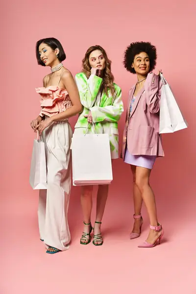 Trois femmes diverses tenant des sacs à provisions sur un fond de studio rose. — Photo de stock