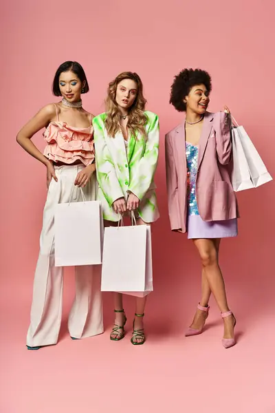 Trois femmes diverses debout à côté de l'autre, souriant, et tenant des sacs à provisions sur un fond rose. — Photo de stock