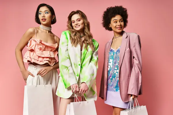 Three women of diverse backgrounds standing together, holding shopping bags against a vibrant pink backdrop. — Stock Photo