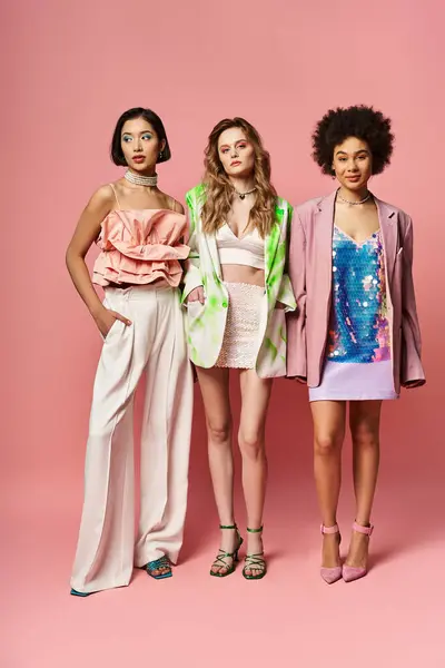 Tres mujeres impresionantes de diferentes etnias se paran lado a lado contra un vibrante telón de fondo rosa. - foto de stock