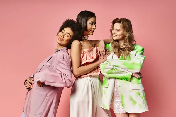 Three diverse women, one Caucasian, one Asian, and one African American, standing stylishly in front of a pink background. — Stock Photo