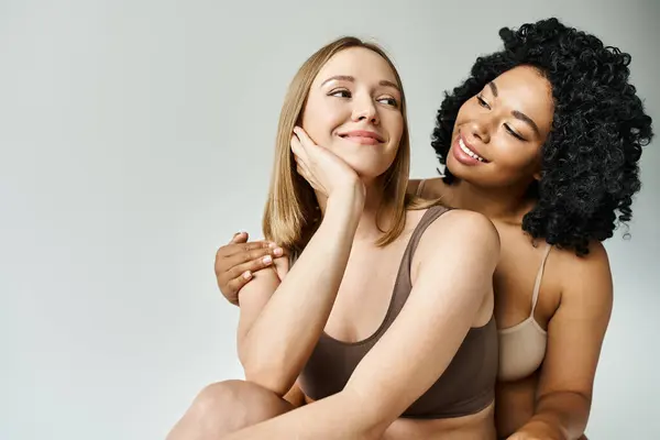 Dos hermosas mujeres diversas en ropa interior de pastel acogedor posando juntos para una imagen. - foto de stock