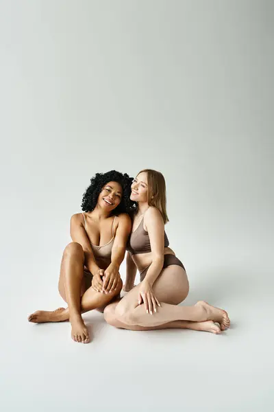 Deux femmes en sous-vêtements pastel confortables, assises sur le sol et posant pour une photo. — Photo de stock