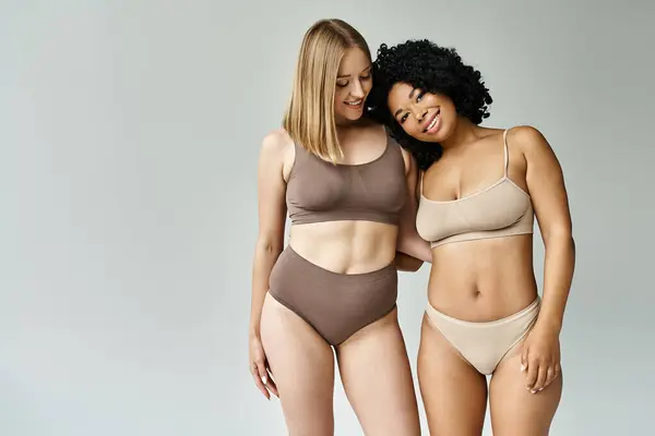 Two beautiful women of different backgrounds standing closely together in cozy pastel underwear. — Stock Photo