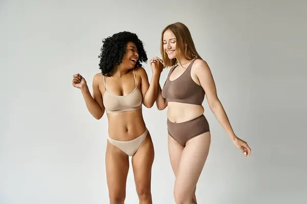 Deux femmes diverses se tiennent côte à côte dans des sous-vêtements pastel confortables, respirant confiance et confort. — Photo de stock