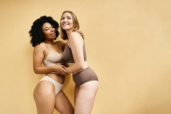 Zwei schöne unterschiedliche Frauen stehen nebeneinander in kuscheliger Pastellunterwäsche. — Stockfoto