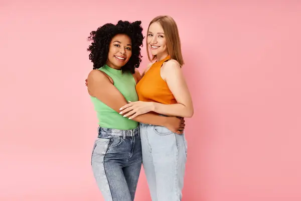 Two attractive diverse women in cozy attire share a heartfelt hug in front of a pink backdrop. — Stock Photo