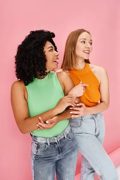 Two attractive women standing together in front of a pink wall. — Stock Photo