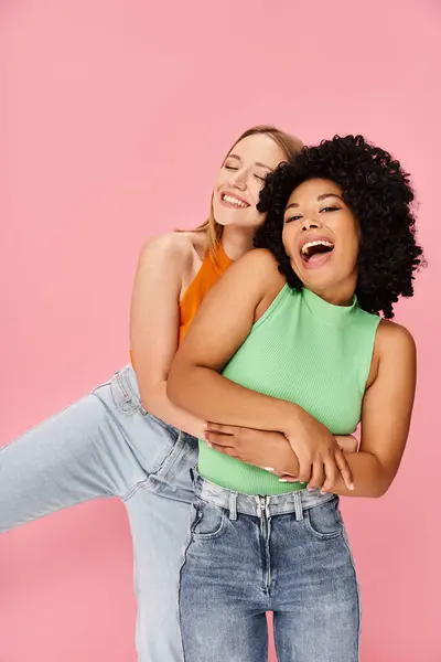 Two young women hug in front of a pink background. — Stock Photo