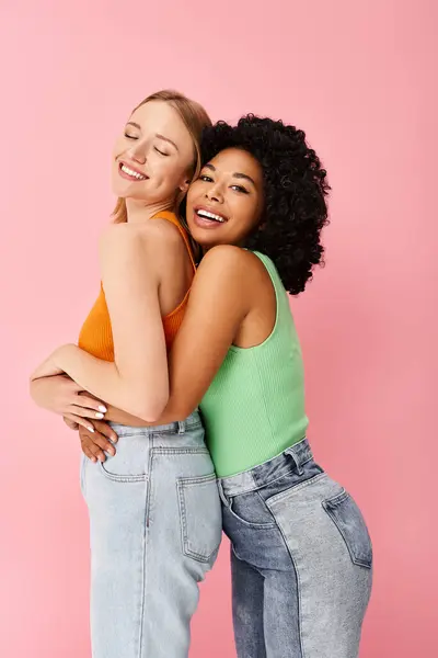 Two attractive diverse women wearing cozy casual attire hugging each other affectionately in front of a vivid pink backdrop. — Stock Photo