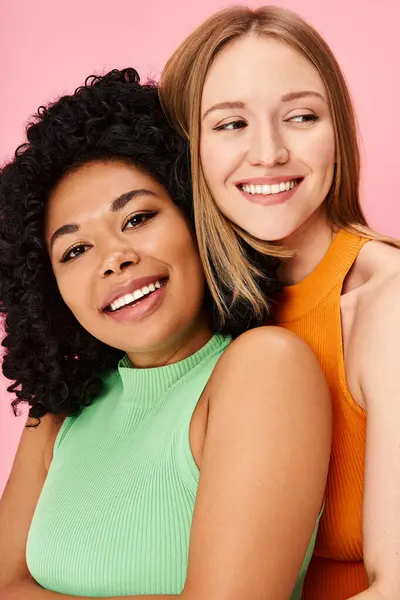 Two women in cozy attire hugging against a pink background. — Stock Photo