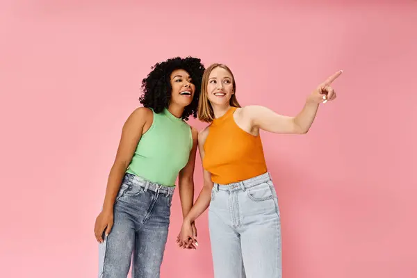 Two attractive diverse women in cozy casual attire standing together in front of a vibrant pink background. — Stock Photo