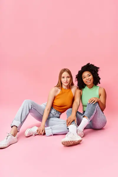 Two women in casual attire posing on the ground for a picture. — Stock Photo