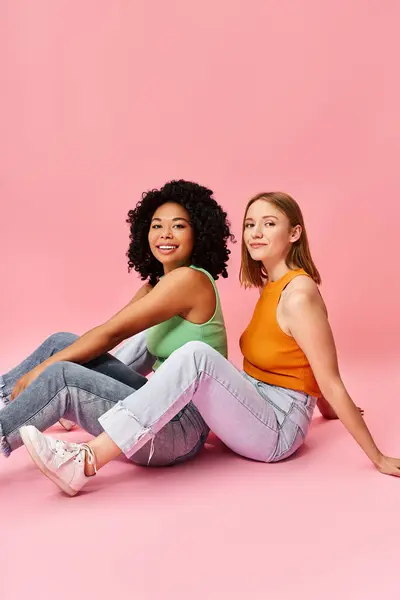 Two diverse women in cozy attire sitting on the ground, posing for a picture. — Stock Photo