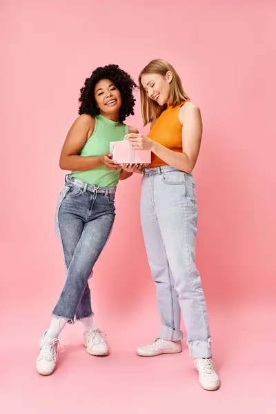 Zwei unterschiedliche Frauen in legerer Kleidung stehen nebeneinander vor einer leuchtend rosa Kulisse. — Stockfoto