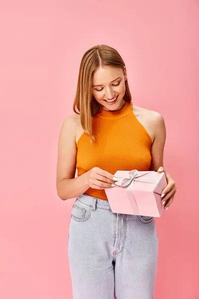 Uma mulher em um top laranja segura uma caixa de presente rosa, exalando calor e emoção. — Fotografia de Stock