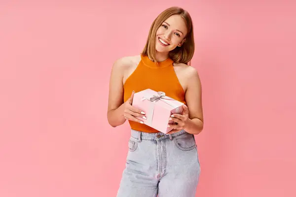 A woman in casual attire, holding a pink gift box, smiling warmly. — Stock Photo