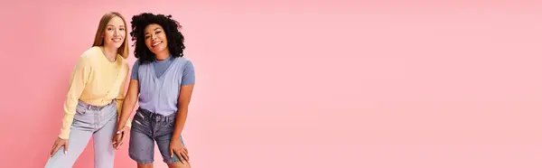 Dos mujeres jóvenes con un atuendo acogedor se paran juntas frente a un fondo rosa. — Stock Photo