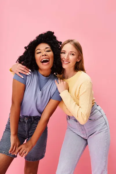 Two diverse women standing confidently in cozy casual attire against a pink backdrop. — Stock Photo