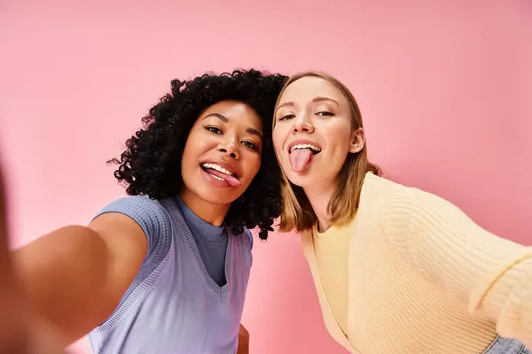 Deux femmes en tenue décontractée prenant un selfie devant un mur rose. — Photo de stock