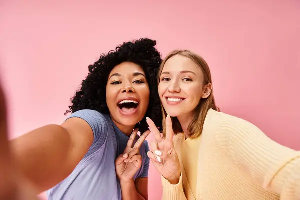 Two women in casual attire pose for a selfie in front of a pink wall. — Stock Photo