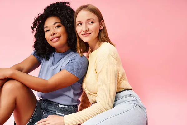 Two attractive women sit comfortably on a pink background. — Stock Photo