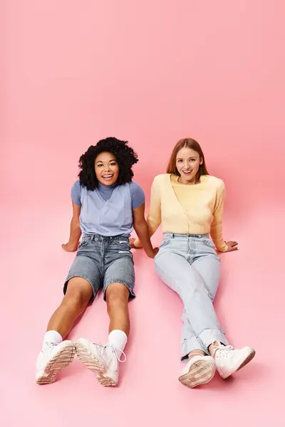 Duas mulheres diversas em traje casual sentado em um fundo rosa, posando para uma foto. — Fotografia de Stock