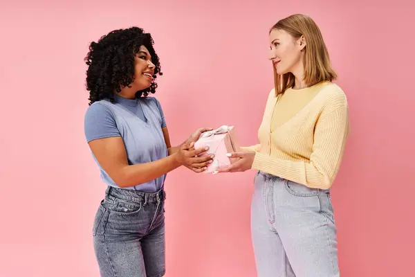 Zwei unterschiedliche Frauen in legerer Kleidung stehen zusammen und tauschen lächelnd ein Geschenk aus. — Stockfoto