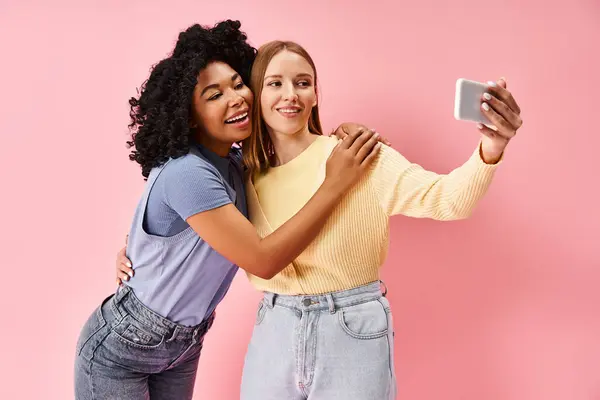 Deux femmes attrayantes et diversifiées en tenue décontractée confortable prenant un selfie avec un téléphone portable. — Photo de stock