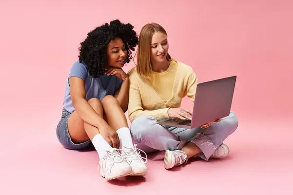 Two diverse women in casual attire sitting on floor, engrossed in laptop. — Stock Photo