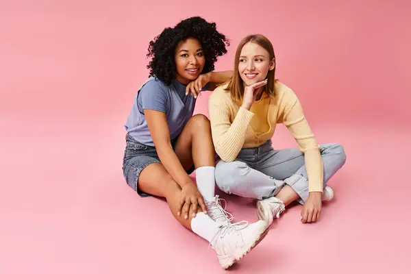Two attractive diverse women in casual attire sitting on ground, striking poses for a picture. — Stock Photo