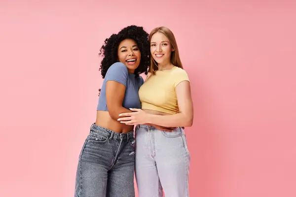 Two diverse women in cozy casual attire stand side by side on a pink background. — Stock Photo