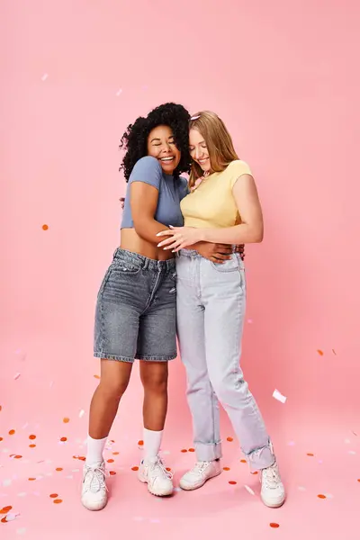 Zwei attraktive, vielfältige Frauen umarmen sich herzlich vor sanftem rosa Hintergrund. — Stockfoto