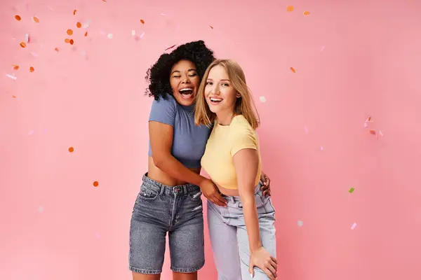Дві привабливі молоді жінки в затишному одязі стоять поруч один з одним на яскравому рожевому фоні. — стокове фото